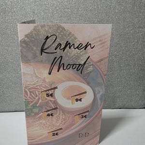 Könnte beinhalten: Eine gefaltete Karte mit einer Aquarellillustration von Ramen mit einem Ei. Die Karte trägt die Worte "Ramen Mood" in einer handschriftlichen Schriftart. Preisetiketten sind auf der Ramen-Schüssel platziert.