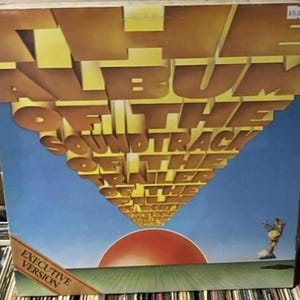 Può includere: Copertina dell'album per "The Soundtrack of the Trailer of the Night Flight" con un grande testo 3D. La copertina presenta un cielo blu, un sole rosso e una figura stilizzata. Le parole "Executive Version" sono visibili.