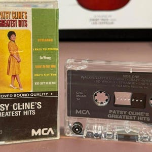 May include: A vintage Patsy Cline's Greatest Hits cassette tape and case. The case features a photo of Patsy Cline in a yellow dress. The cassette tape is clear with a black label. The album title and song titles are visible.