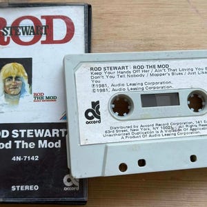 以下が含まれることがあります： ロッド・スチュワートのアルバム「Rod The Mod」のヴィンテージカセットテープとケース。ケースにはアルバムタイトルとロッド・スチュワートの肖像画が描かれています。カセットテープは薄いグレーで、アルバムタイトルと曲目が記載されています。