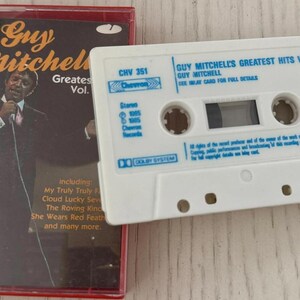 May include: A vintage cassette tape and case featuring Guy Mitchell's Greatest Hits Vol. 1. The cassette is white with blue text, and the case is red with a photo of Mitchell. The case includes song titles like "My Truly Truly Fair" and "Cloud Lucky Seven."