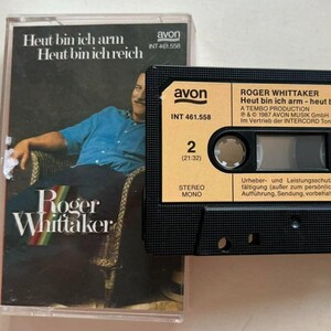 May include: A vintage cassette tape and case featuring Roger Whittaker's album "Heut bin ich arm - Heut bin ich reich." The cassette case has a photo of Roger Whittaker. The cassette tape is black with orange and white labels. The album is a stereo recording.