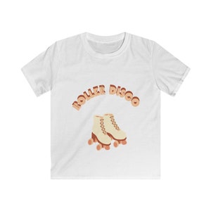 Puede incluir: Camiseta blanca con la frase "ROLLER DISCO" en una fuente retro sobre un gráfico de patines de ruedas color crema con ruedas naranjas. La camiseta es de cuello redondo.
