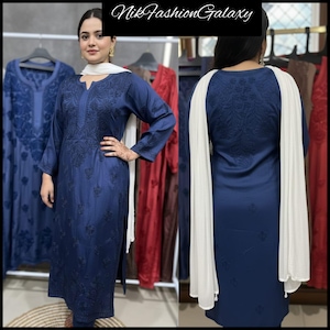 Può includere: Un completo tunica e pantaloni ricamati blu navy con una sciarpa bianca. La tunica presenta ricami floreali intricati e uno scollo a V. L'outfit è esposto su un appendiabiti con altri capi. Il testo "Nik Fashion Galaxy" è nella parte superiore dell'immagine.