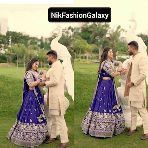 May include: A couple in formal wear, posing outdoors. The woman is in a royal blue lehenga with gold embroidery. The man wears a cream-coloured suit. The image includes the text "NikFashionGalaxy".