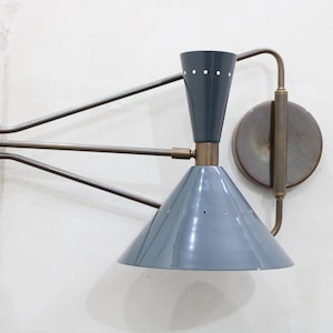 May include: A wall-mounted lamp with a blue-gray conical shade and a dark gray upper section. The lamp features a brass-colored arm and mounting hardware. The design is mid-century modern.