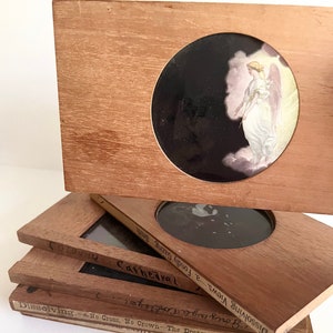 May include: A stack of wooden slide frames with glass inserts. The top frame features a black and white image of an angel with wings. The bottom frame has the text "Dissolving.-e-No Cross, No Crown The Dreamer. CASTLE OF ST. ANGELO. Daylight." printed on it.