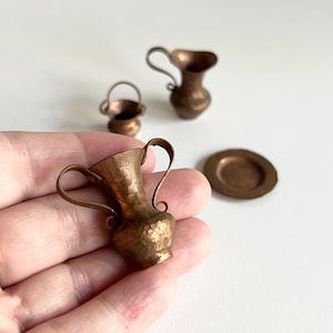 Peut inclure: Ensemble de quatre articles de cuisine miniatures en cuivre, comprenant un pichet, un bol, un vase et une assiette. Les articles sont tous en cuivre martelé et ont un aspect rustique et antique.