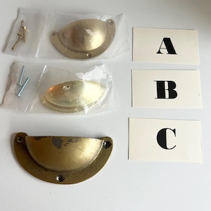 May include: Three brass cabinet knobs in different sizes and finishes. The knobs are packaged in clear plastic bags. The bags are labelled A, B, and C.