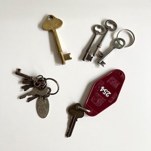 May include: A collection of vintage keys, including a brass key with a heart-shaped head, a set of keys with a keychain, and a red motel key with the number "254" printed on it.