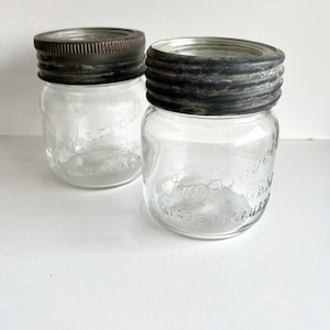 May include: Two clear glass jars with metal lids. The lids are embossed with the text "Improved" and "Made in Canada".