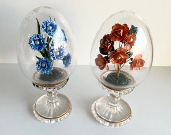 May include: Two glass dome paperweights with floral arrangements. One paperweight features blue flowers and the other features orange flowers.