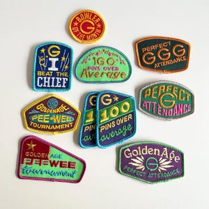 May include: Nine embroidered patches with various colors and designs. The patches feature text such as "Golden Age Pee-Wee Tournament", "Perfect Attendance", "Beat the Chief", and "100 Pins Over Average".