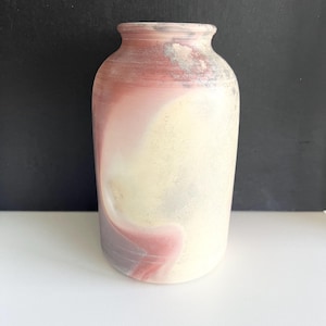 May include: A cylindrical ceramic vase with a wide base and a narrow neck. The vase features a blend of colours, including shades of red, pink, yellow, and grey. The colours are swirled together, creating a marbled effect. The vase is suitable for home decor.