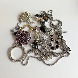 Puede incluir: Una colecci&oacute;n de joyas de plata y pedrer&iacute;a, que incluye pendientes, broches y collares. Las joyas presentan una variedad de formas y tama&ntilde;os, incluyendo corazones, flores y dise&ntilde;os geom&eacute;tricos. Las piezas est&aacute;n dispuestas en una pila sobre un fondo blanco.