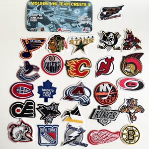 May include: A selection of NHL team crest patches, featuring logos for teams such as the St. Louis Blues, Dallas Stars, and Toronto Maple Leafs. The image also includes a Molson NHL Team Crests II card.