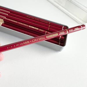 Peut inclure: Un ensemble de crayons de couleur rouge dans un étui en plastique transparent. Les crayons sont étiquetés "A.W.FABER-CASTELL Thin Color 7490 GERMANY" et "DARK 626 CARMINE". Les crayons sont parfaits pour le marquage d'impression.