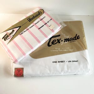 May include: Two pink and white striped pillowcases packaged with a white sheet. The pillowcases are labelled "Tex-made Woodward's" and "Two Pillow Cases Select Quality, Finished Size 42 x 33". The sheet is labelled "Tex-made, Made right here in Canada by Dominion Textile Company Limited, One Sheet Un Drap".