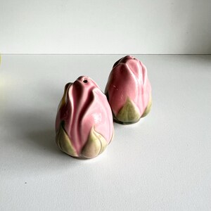 May include: A set of two pink ceramic salt and pepper shakers shaped like rose buds with green leaves.