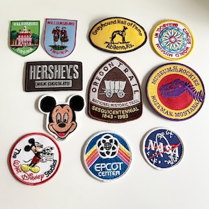 以下が含まれることがあります： チョコレートバー、国立公園、博物館、サーカス、宇宙機関、テーマパークなど、さまざまなテーマの刺繍パッチ10個のセット。パッチはすべて円形または楕円形で、白い縁取りがされています。