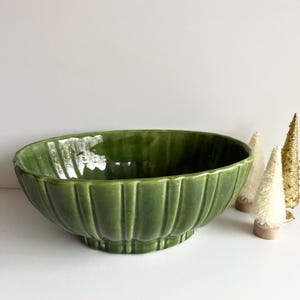 May include: A large, green ceramic bowl with a fluted design. The bowl is oval shaped and has a wide, shallow base.