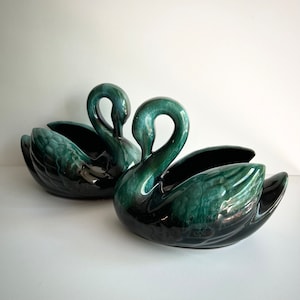 May include: Two ceramic swan planters in a dark green and black glaze. The swans are facing each other with their necks curved.