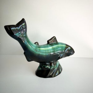 May include: A ceramic fish figurine with a blue and green glaze. The fish is leaping out of the water and has a detailed, realistic design.
