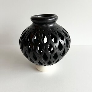 May include: Black ceramic vase with a decorative cut-out design. The vase has a round shape and a small base.