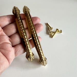 May include: Two gold-toned cabinet door pulls with a rope design. The pulls are 10 cm long and have a 7.5 cm centre-to-centre spacing. The pulls come with four gold-toned screws.