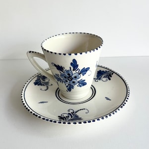 May include: A white teacup and saucer with a blue and white floral design. The cup and saucer have a scalloped edge and a blue dot pattern.