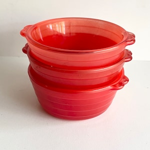 May include: Three red glass bowls with rounded edges and handles. The bowls are stacked on top of each other.