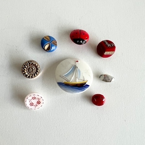 May include: Assortment of colourful buttons with various designs, including a ladybug, a sailboat, a floral pattern, and a geometric pattern.