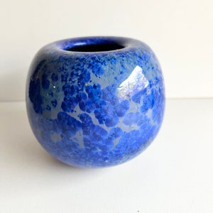 May include: A round blue ceramic vase with a white speckled glaze. The vase has a wide opening and a smooth, rounded bottom.