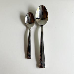 May include: Two silver spoons, one larger than the other, with rounded bowls and simple, squared handles.