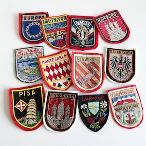 May include: A selection of embroidered patches, each depicting a different city or country. The patches feature detailed designs, such as landmarks, flags, and text, in a variety of colours. These patches are likely vintage or souvenir items, perfect for collecting or customising clothing.