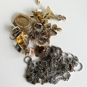 Puede incluir: Una colecci&oacute;n de joyas de oro y plata, que incluye cadenas, pendientes, broches y gemelos. Las joyas est&aacute;n dispuestas en una pila sobre una superficie blanca.