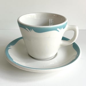 以下が含まれることがあります： 縁に薄い青色の帯が付いた白い陶器のティーカップとソーサー。帯は波打つようなデザインです。