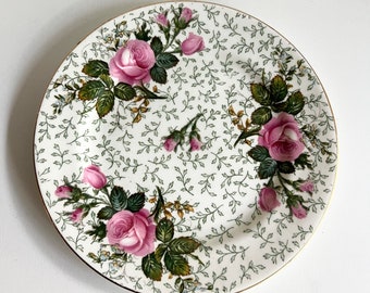 May include: A white ceramic plate with a gold rim features a delicate floral pattern of pink roses and green leaves on a white background.