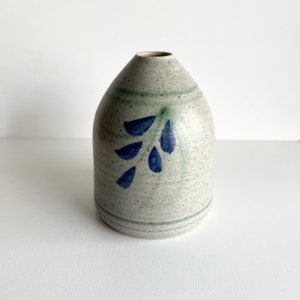 May include: A small, grey ceramic vase with a blue and green floral design. The vase has a rounded body and a narrow opening.