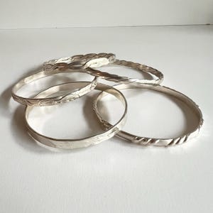 May include: Set of four silver bangles, one with a braided design, one with a floral pattern, and two with a smooth finish.