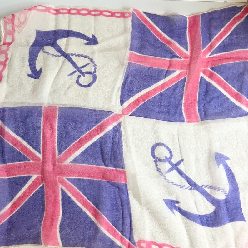 May include: A white fabric scarf with a repeating pattern of anchors and the Union Jack flag in pink and purple.
