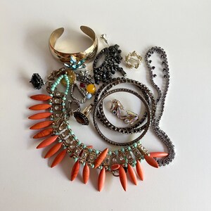 Puede incluir: Una colecci&oacute;n de joyas con una variedad de estilos y colores, que incluye un brazalete de oro, un collar de cuentas turquesa y naranja, y varios pares de aretes.