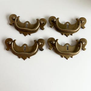 May include: Four antique brass drawer pulls with ornate designs and keyhole cutouts.