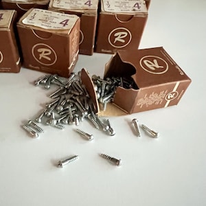 May include: A collection of brown cardboard boxes labelled with the letter R, containing silver-coloured metal wood screws. One box is tipped over, spilling numerous small, threaded fasteners onto the surface. Each box is marked 1/2 inch size 4.