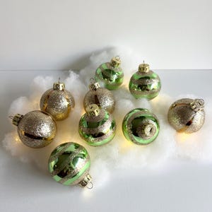 May include: A set of ten vintage Christmas ornaments with a green and gold glitter finish. The ornaments have a striped pattern and are perfect for adding a touch of retro charm to your holiday decor.