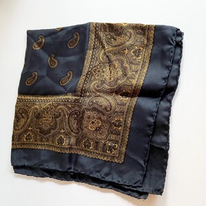 May include: A black silk scarf with a gold paisley pattern. The scarf has a fringed edge.