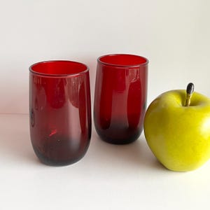 May include: Two red glass tumblers on a white surface next to a green apple.