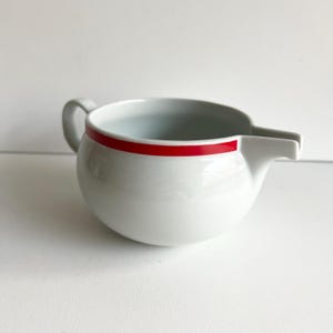 May include: White ceramic gravy boat with a red stripe around the rim.