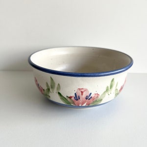 May include: A white ceramic bowl with a blue rim and a floral design featuring pink flowers and green leaves.