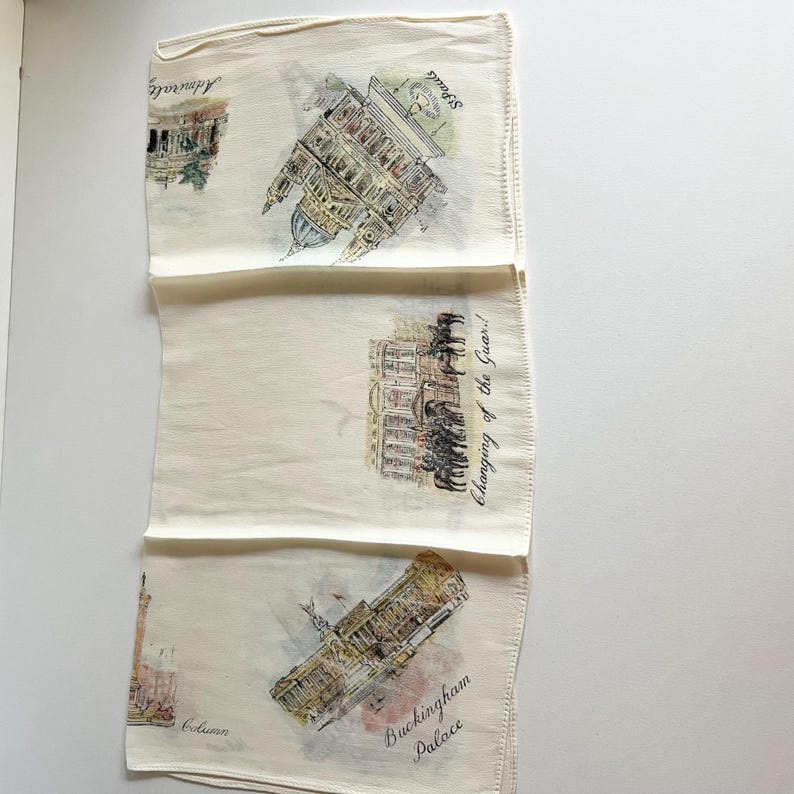 May include: A white cotton handkerchief featuring a watercolour design of London landmarks. The design includes Buckingham Palace, the Houses of Parliament, and the Changing of the Guard ceremony.